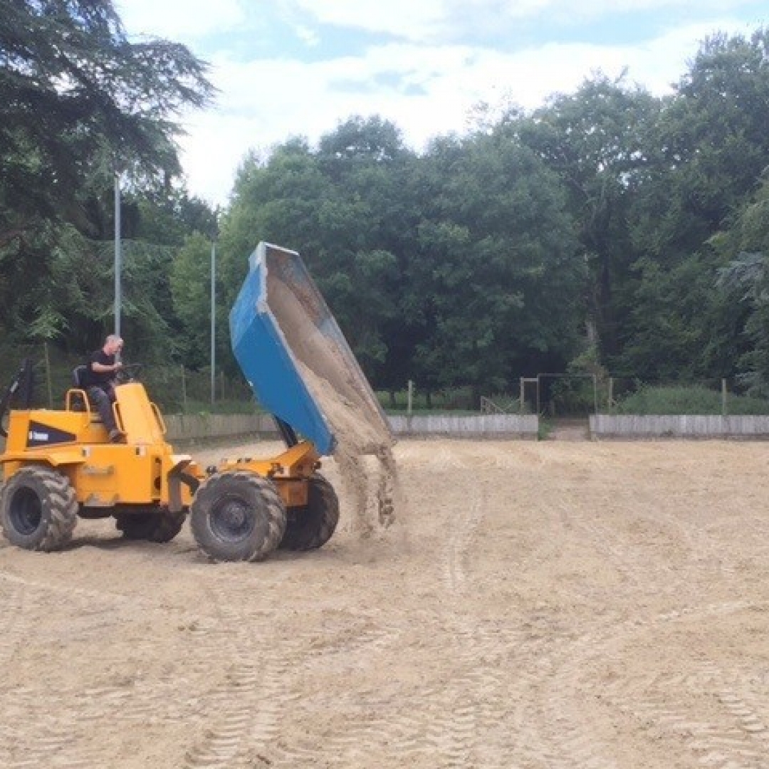 yellow dumper truck tipping sand into a horse riding arena