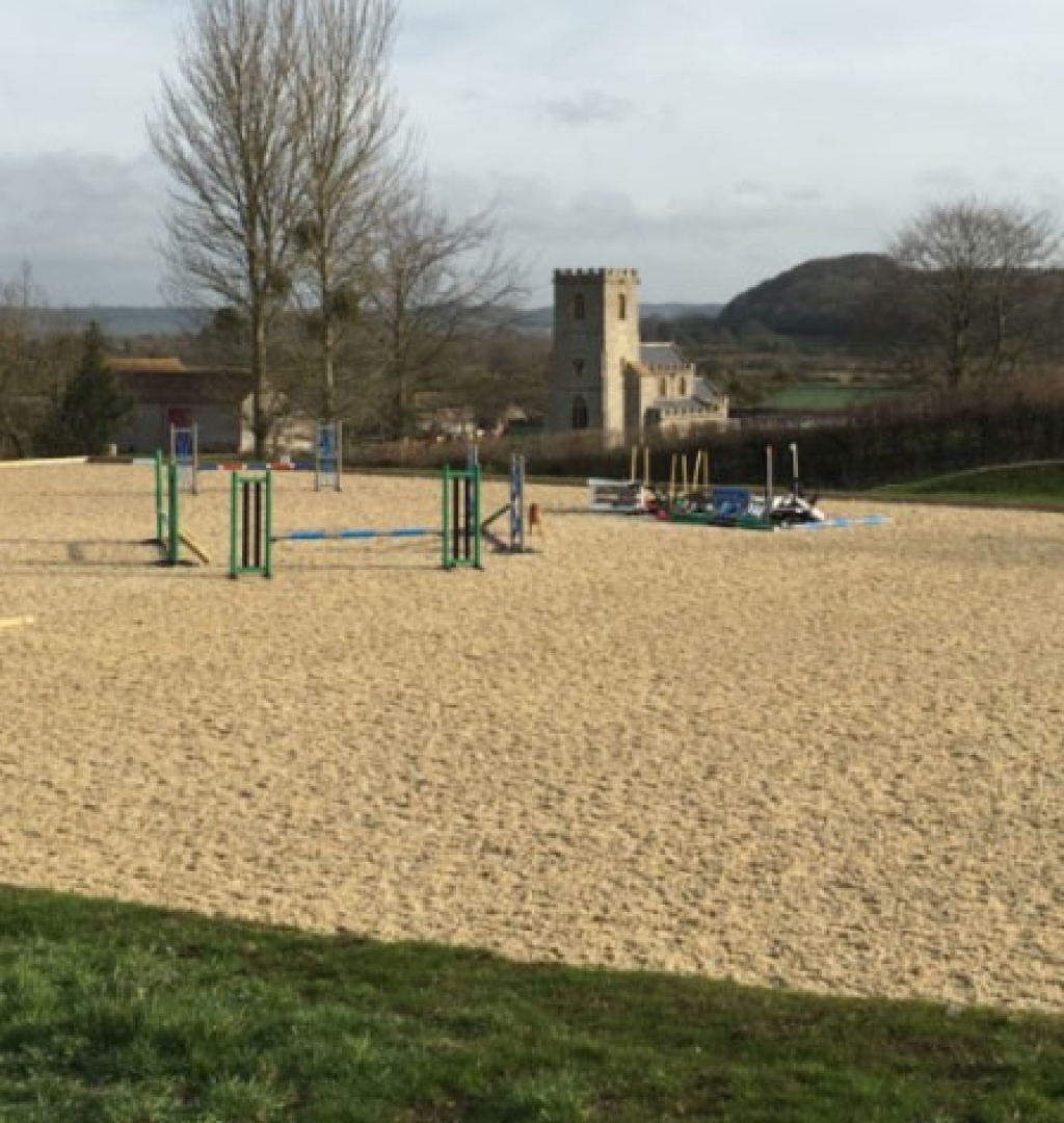 large outdoor riding arena set in English countryside with a church in the background